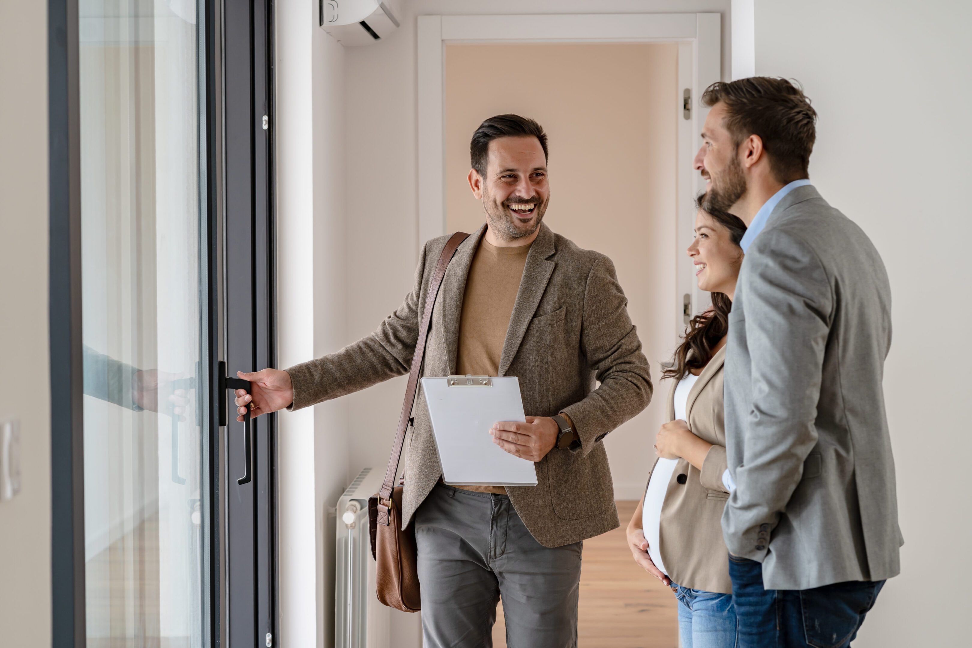 Young married couple talking with a real-estate agent visiting apartment for sale or for rent. Future parents buying an apartment. Real estate concept. A new beginning