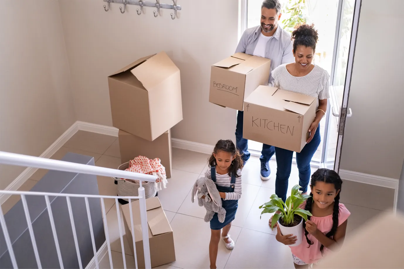 A happy family carrying moving boxes labeled "kitchen" and "bedroom" into their new home in Ottawa, illustrating the guide for first-time home buyers.